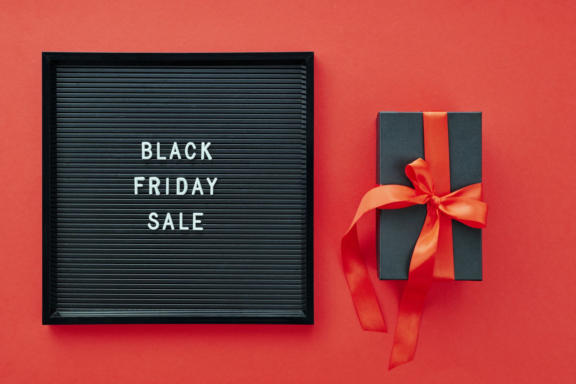 Black Friday sale display with gift box and ribbon on vibrant red surface.