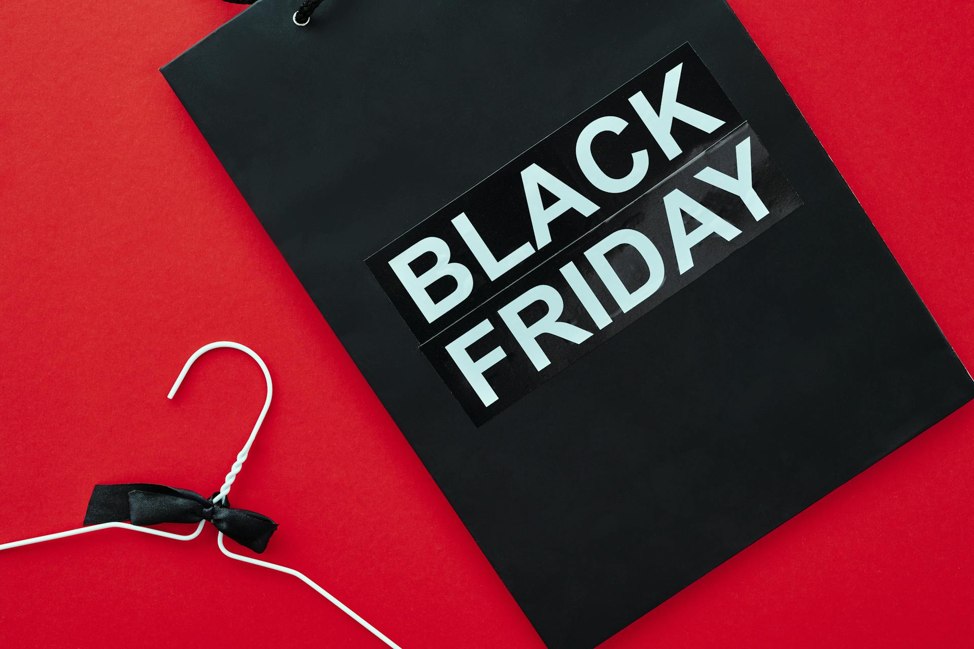 A Black Friday shopping bag and hanger on red background, symbolizing consumerism and retail sales.