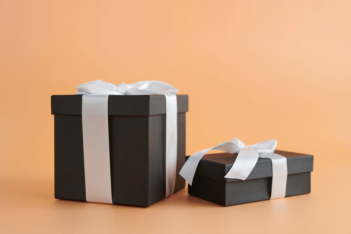 Two elegant black gift boxes with white ribbons on a neutral beige background