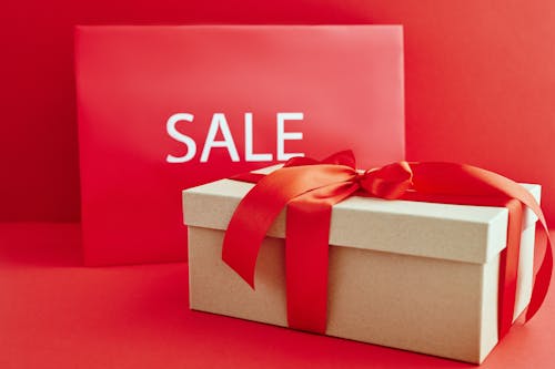 Free Cardboard Box with Red Ribbon Beside A Sale Sign Stock Photo