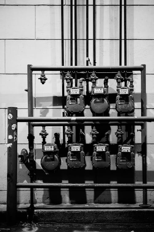 Black and white of aged gas meters attached to thin iron pipes near wall