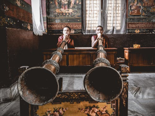 Man Tibetan musicians playing dungchen instrument in temple