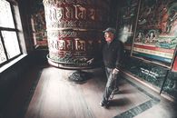 Full body contemplative elderly Asian male wearing casual outfits walking around prayer wheel in authentic religious temple