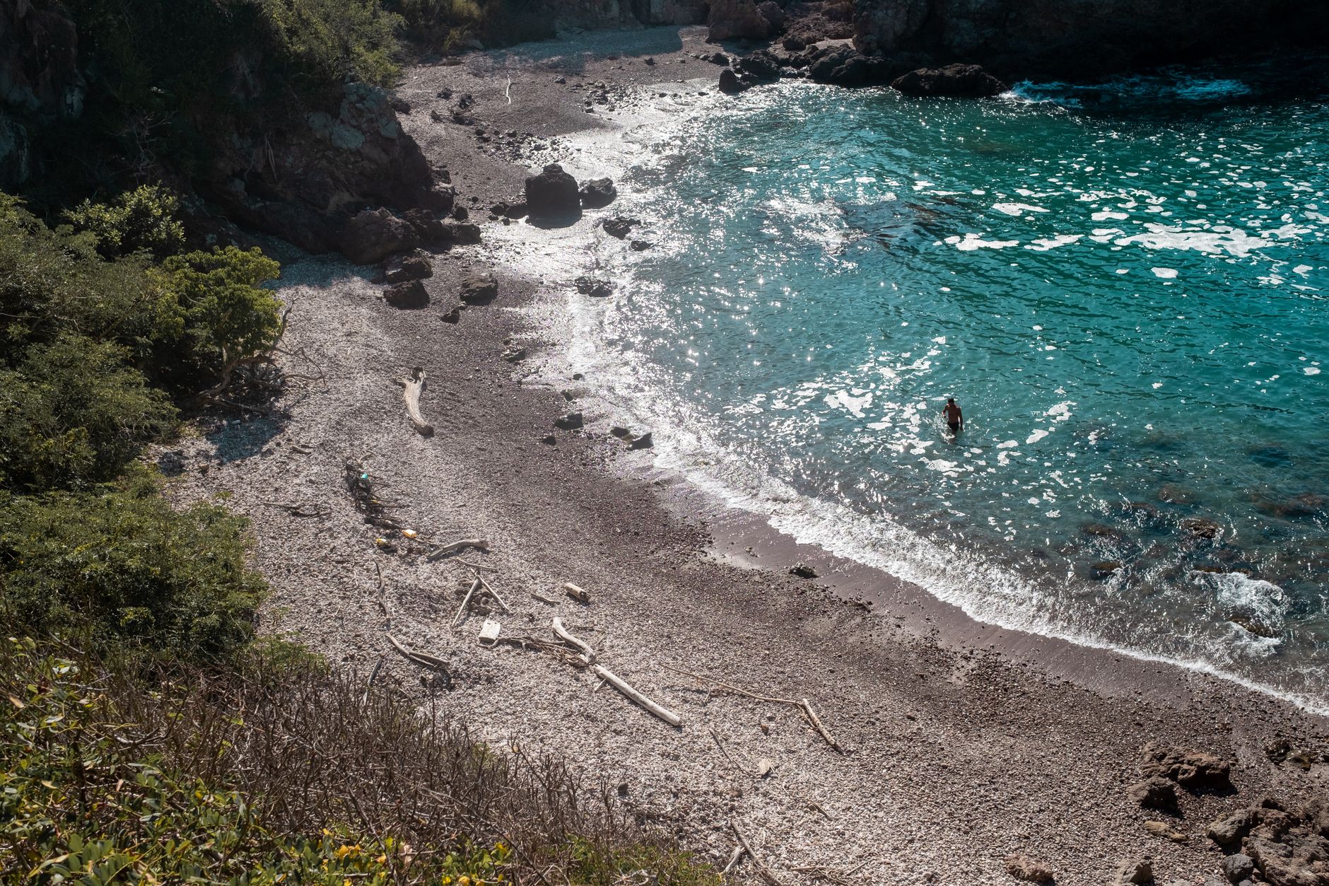 A stunning view of a sunlit bay with turquoise waters and a rocky beach, perfect for a summer vacation.