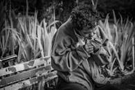 黑白照片里，一位老人坐在公园长凳上点烟