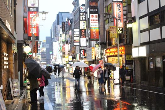 人们打着伞走过东京多雨而充满活力的街道，街道上布满了发光的标志