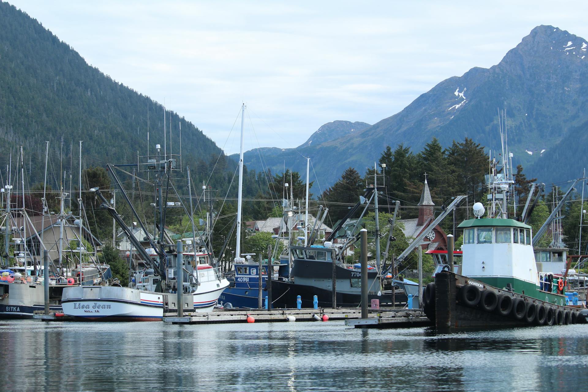Panoramic view of Sitka harbor showcasing docked fishing boats against mountainous backdrop.