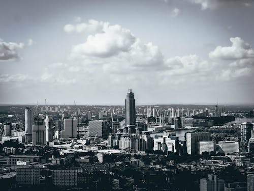 Grayscale Photo of City Buildings Under Cloudy Sky
