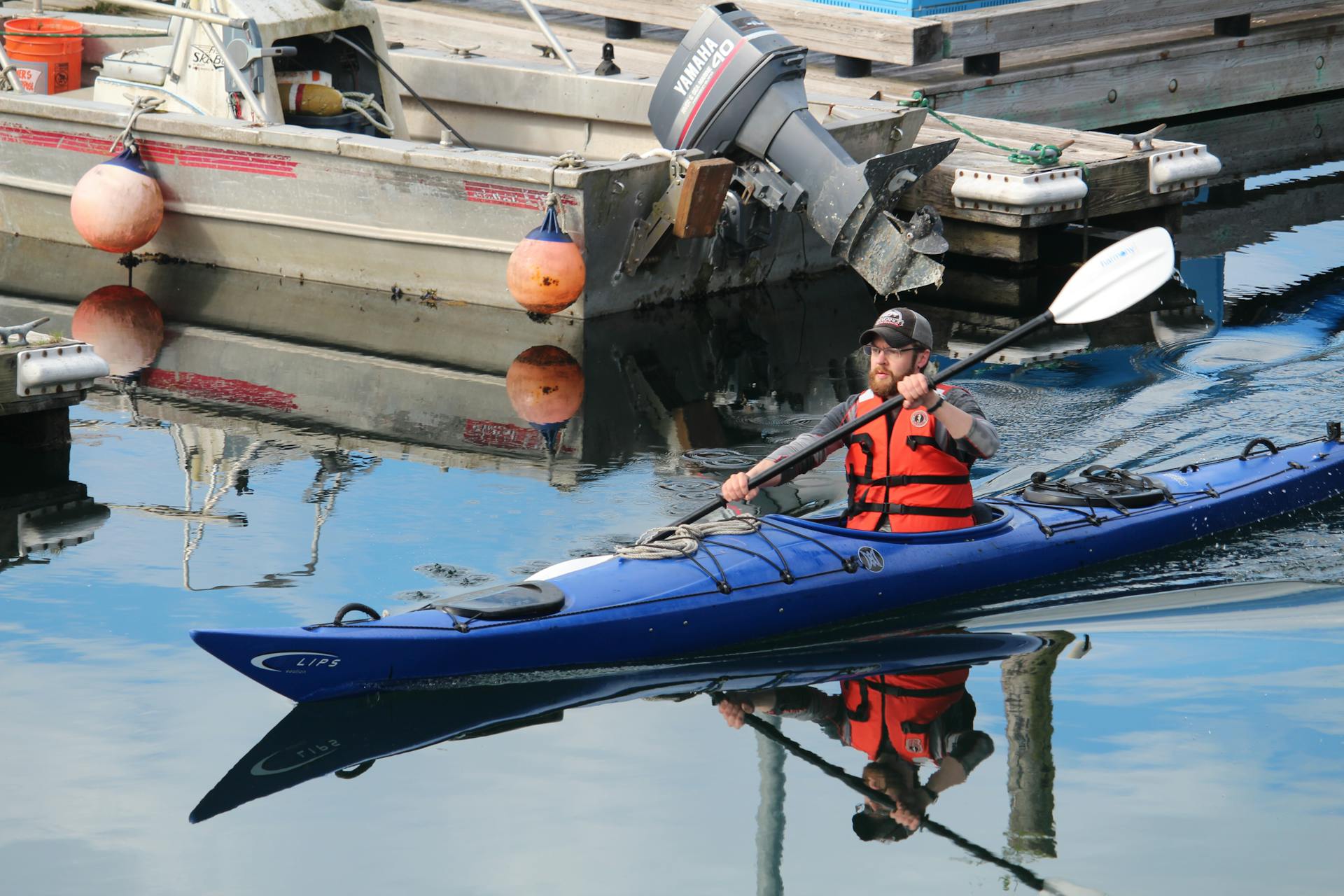 Man kayaking in Sitka, Alaska harbor with vibrant reflections and calm water surface.