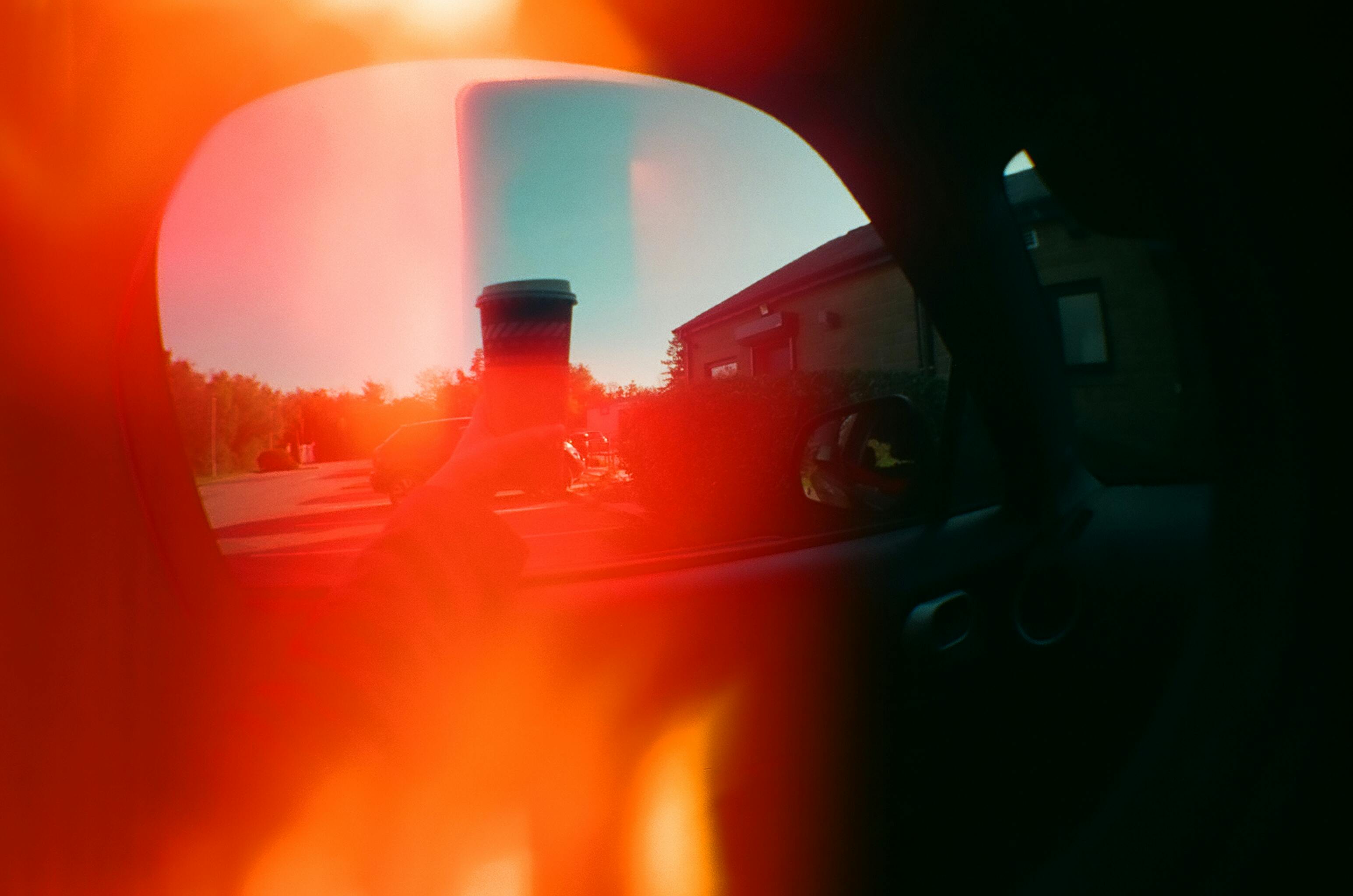 A striking image of a hand holding a coffee cup viewed through a car window with artistic light leaks.