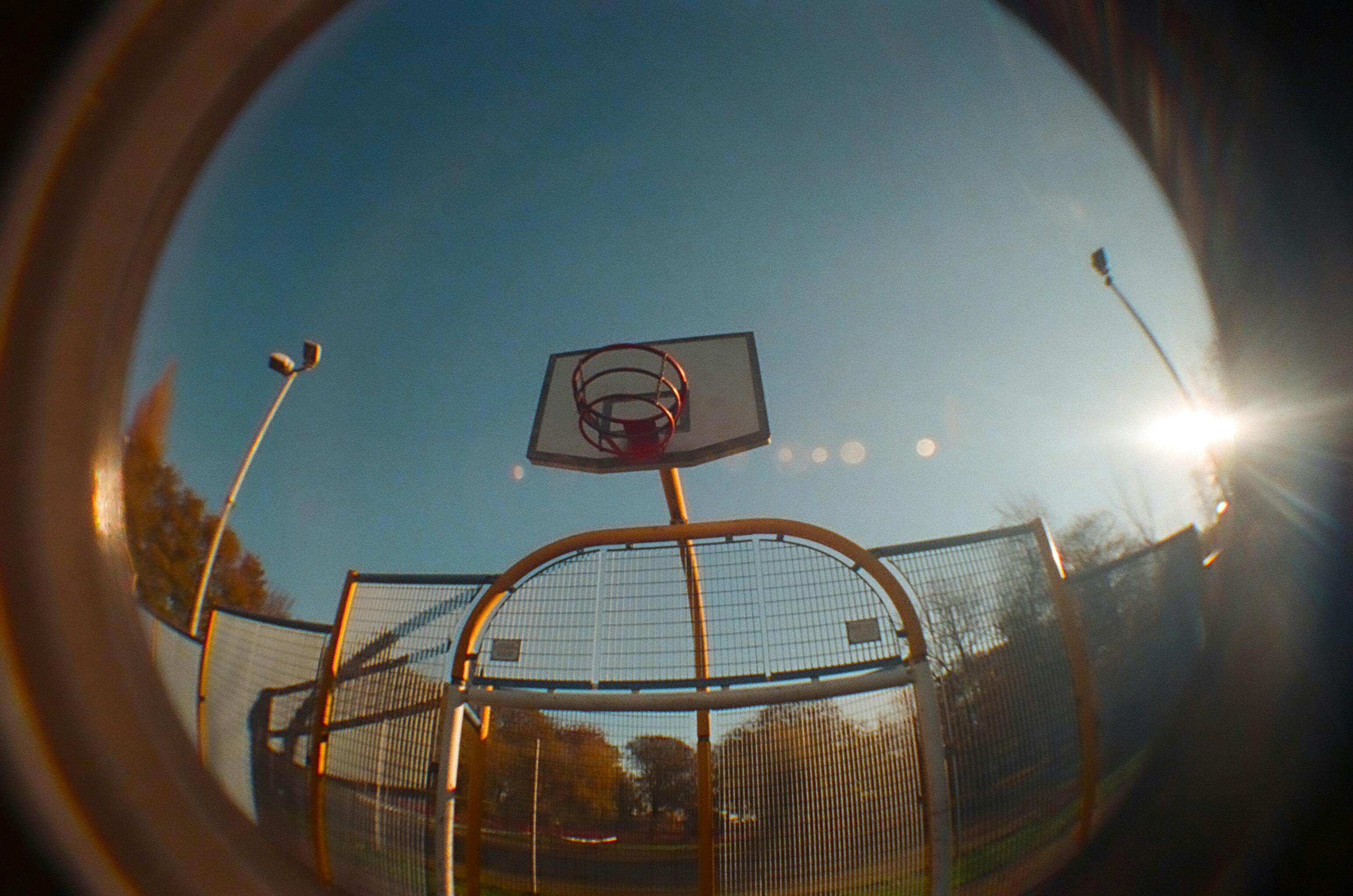 Low angle fisheye shot of a basketball hoop against a clear blue sky in daylight.