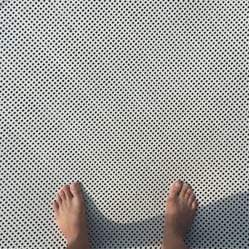 Top-down view of bare feet on a textured grid pattern surface, capturing simplicity and contrast.