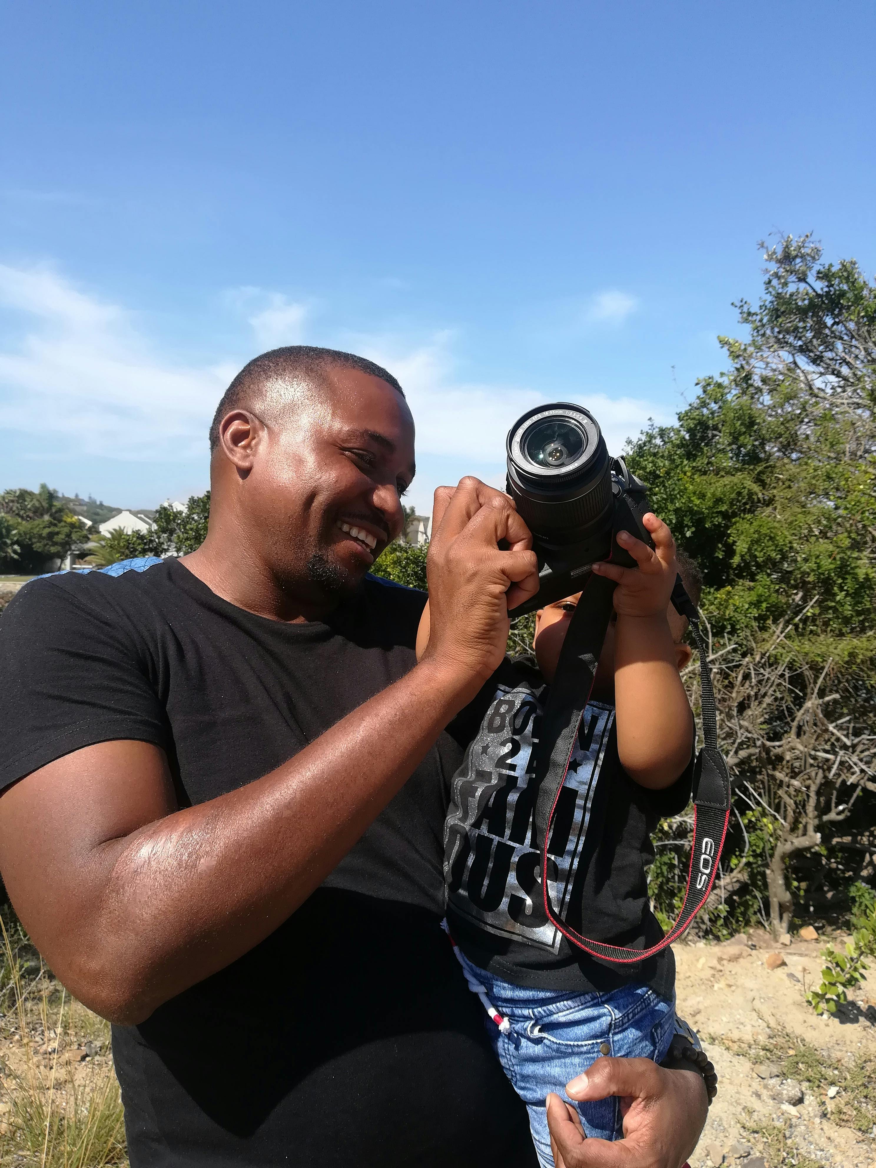 A joyful moment captured of a father teaching his son to use a camera, outdoors in South Africa.