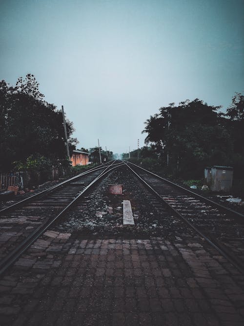 Perspective empty railway tracks with weathered paved crossing running along countryside under blue sky