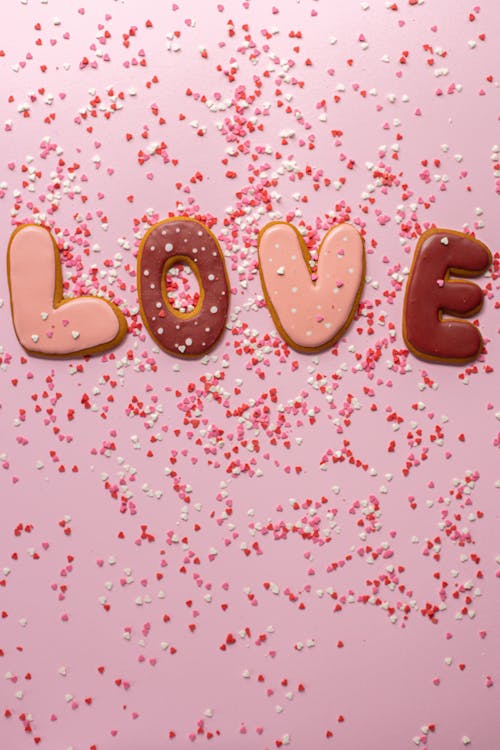 Top view of different colorful handmade cookies with shape of letters with sprinkles creating word love on pink background