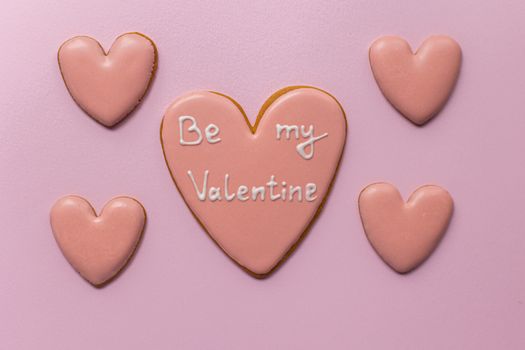 Top view of sweet heart shaped cookies saying Be My Valentine on pink background