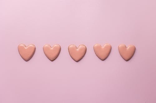 Top view of various handmade small cookies in heart shape placed on pink background next to each other
