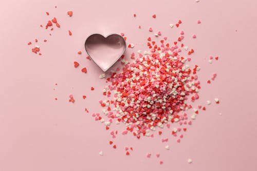 Free Top view of form for cooking in shape of heart near small handful of confetti on pink background Stock Photo
