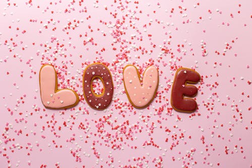 Top view of composed cookies making Love inscription with small heart shaped confetti on pink background