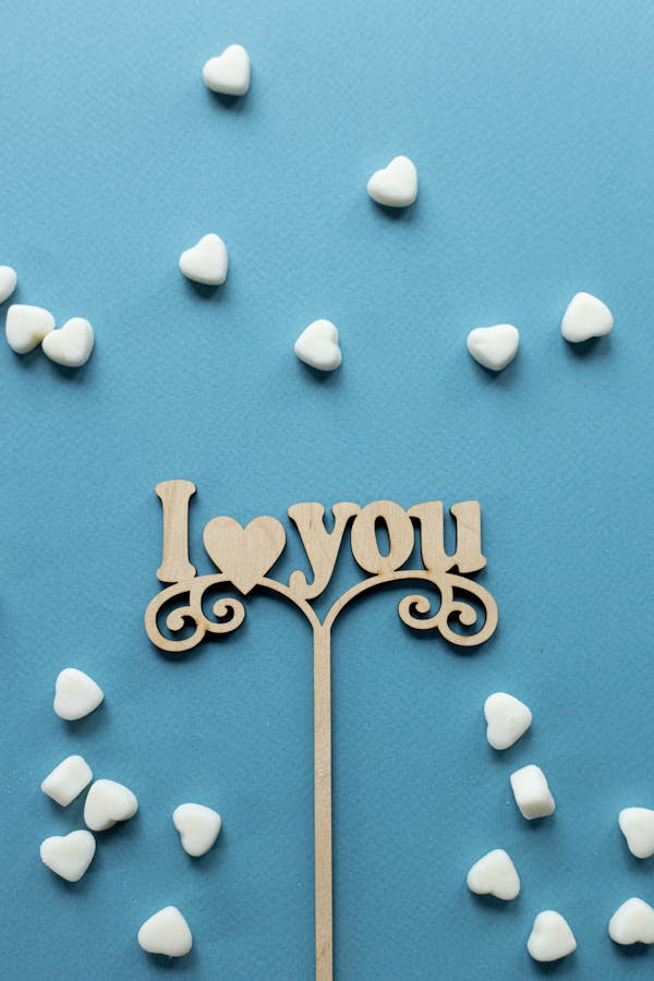 Top view composition of topper in form of declaration of love among heart shaped sugar sprinkles on blue background