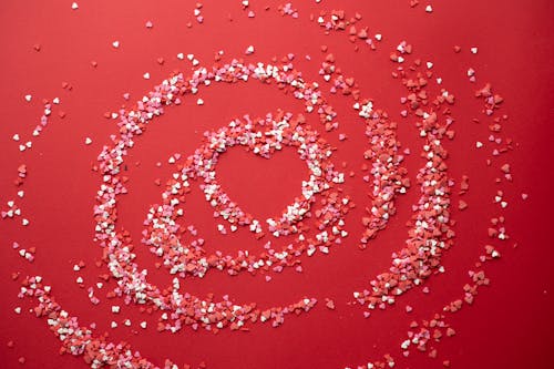 Free Top view of arranged confetti of different colors forming heart for Valentines Day concept on red background Stock Photo