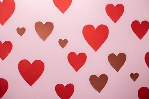 Cutout paper heart stickers glued on pink background symbolizing romantic Valentines Day celebration