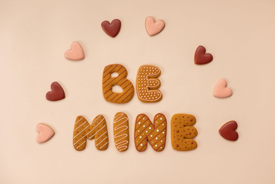 Top view of cookies with frosting forming Be Mine phrase and heart shaped cookies arranged in semicircle on beige background