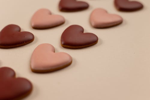 From above of red and pink heart shaped cookies with frosting arranged in rows on beige background during valentines day
