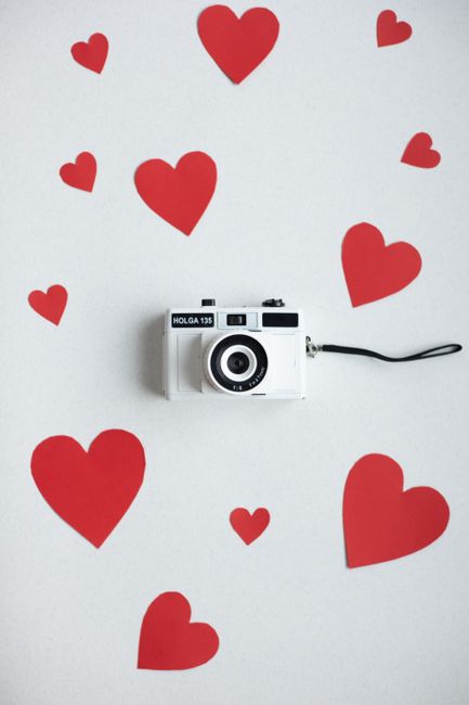 Top view paper cutout of many red hearts scattered on white background with white vintage photo camera on valentines day