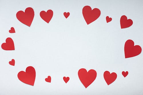 Free Top view paper cutout of different sizes red paper hearts forming oval placed on white background during valentines day celebration concept Stock Photo