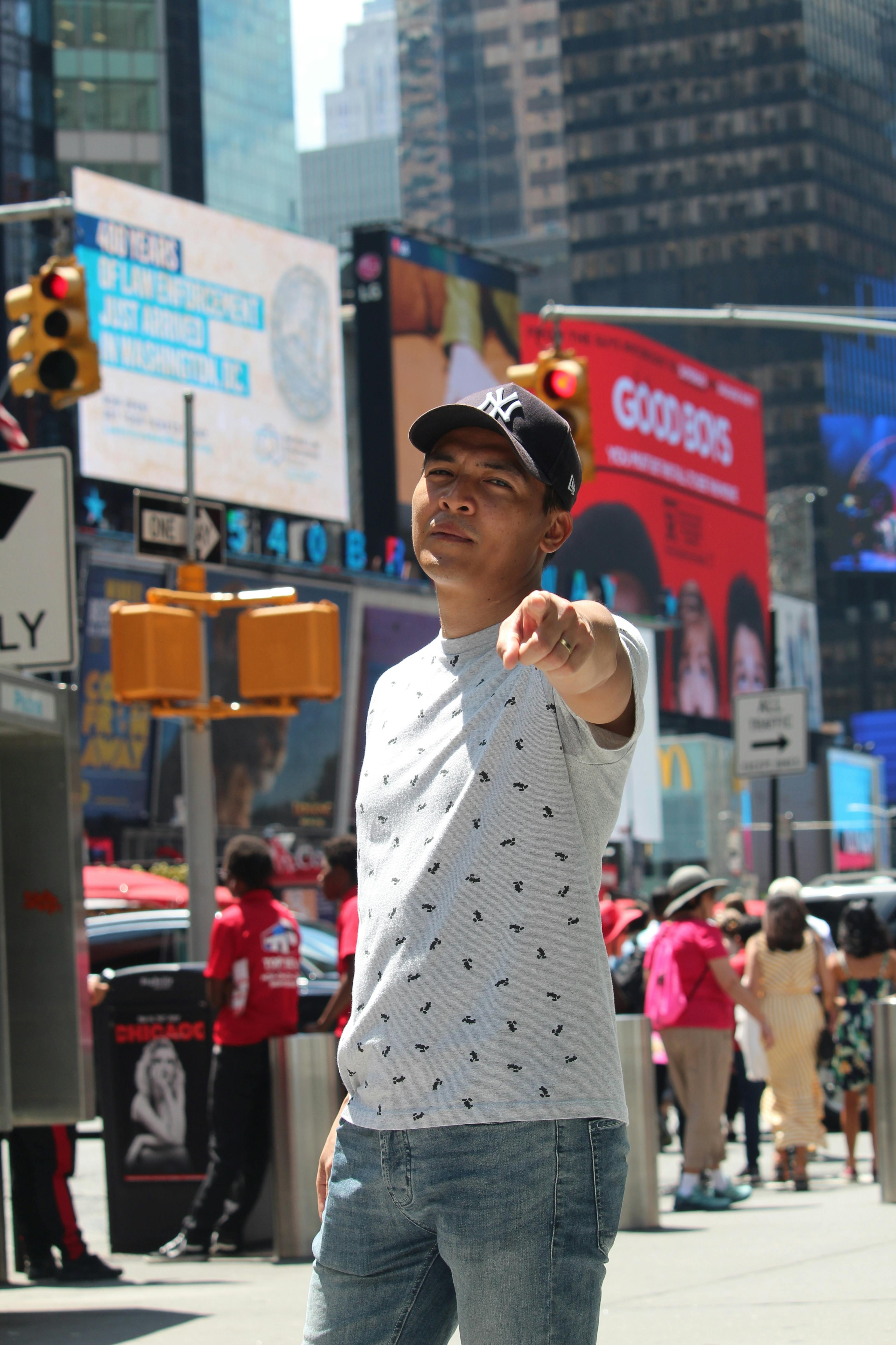 Casual young man pointing at camera, urban backdrop of Times Square, NYC.