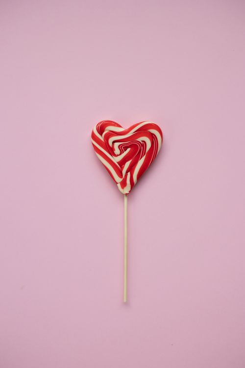 Free Top view of tasty red and white heart shaped lollipop  on wooden stick placed on pink background during holiday celebration Stock Photo