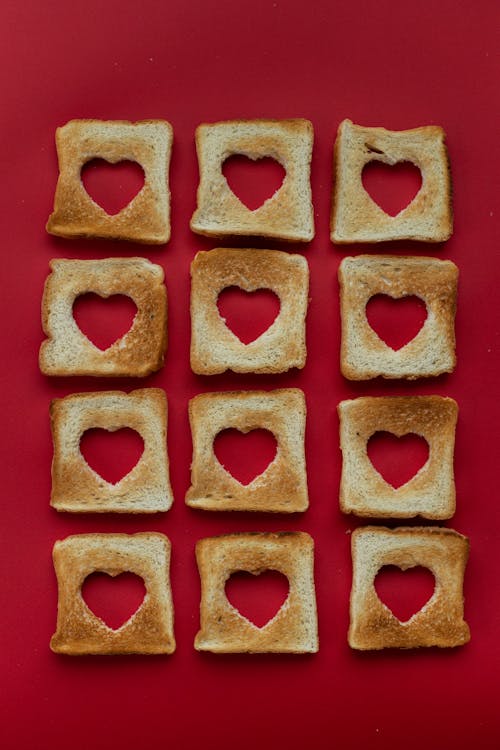 Top view of composition of slices of toasted bread with cut out hearts against red background