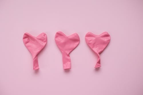 Free Top view of pink deflated balloons in form of hearts placed on pink background in studio Stock Photo