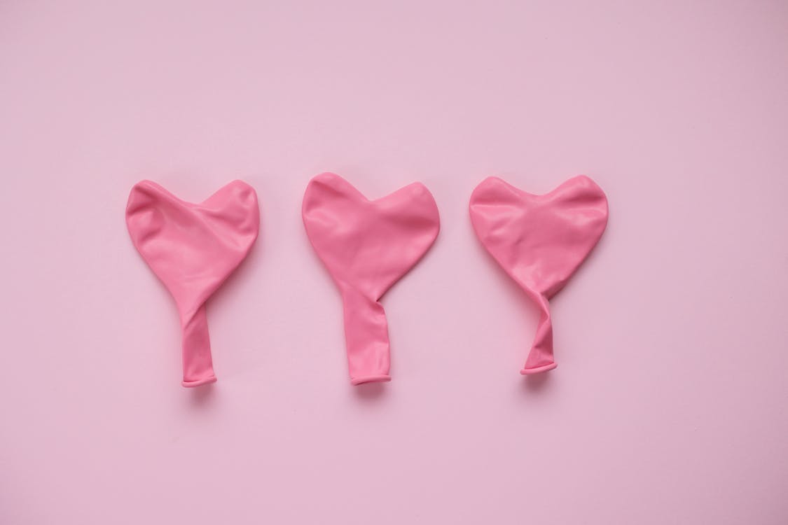 Top view of pink deflated balloons in form of hearts placed on pink background in studio