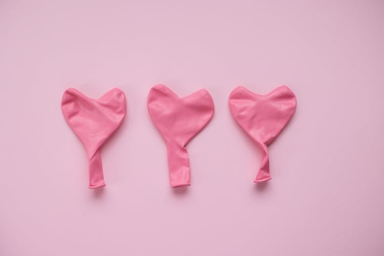Deflated Balloons In Form Of Hearts Against Pink Background
