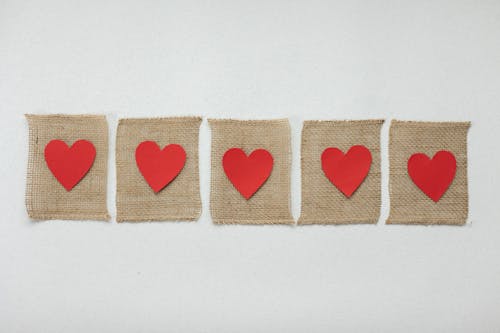 From above of handmade burlap pieces of fabric with bright red hearts placed on white background