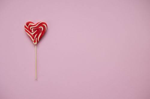 Free From above of colourful tasty lollipop in shape of heart placed on pink background in light studio Stock Photo
