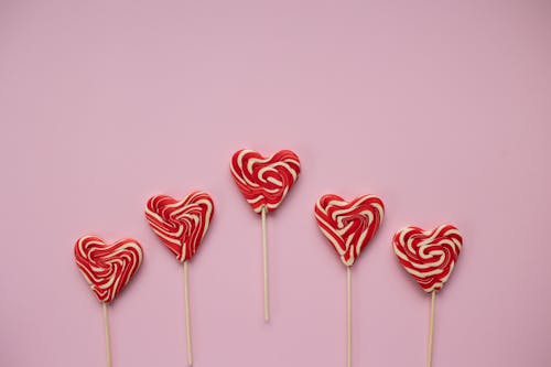 Top view of colorful sweet lollipops in form of hearts placed on pink background in studio