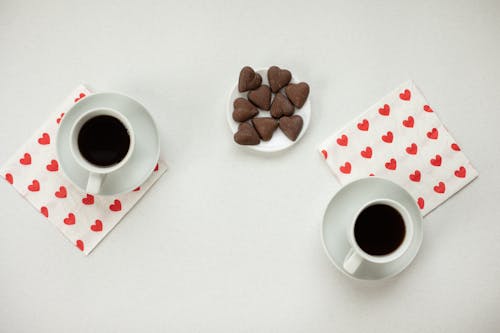 Free Top view of cups with hot coffee and chocolate candies in heart shape on white background Stock Photo