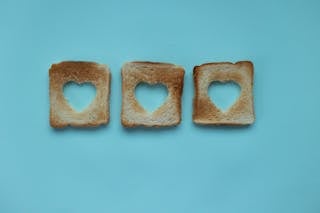 Top view of crusty pieces from toast bread with cut hearts on blue background