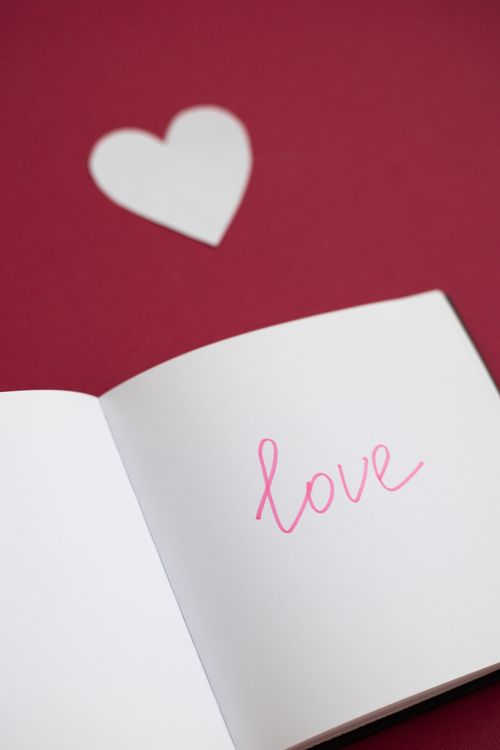 Free High angle of opened notebook with word and cutout paper heart on red background Stock Photo