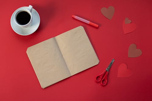 Top view of craft papers near scissors and cup of hot coffee on red background