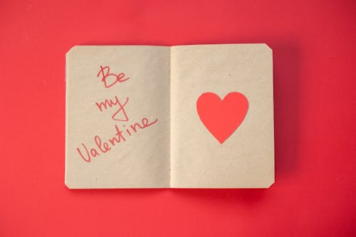 Top view of romantic phrase written on craft paper of notepad with heart placed on red background during Saint Valentines day