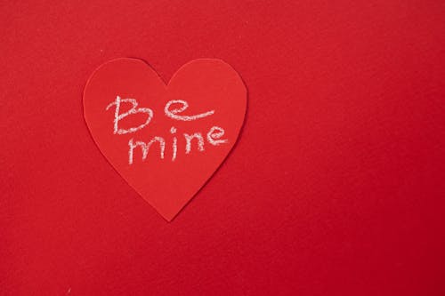 Top view of Be Mine phrase written on heart shaped piece of paper placed on table during Saint Valentines day celebration