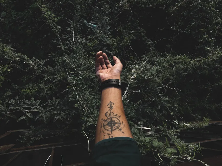 Tatouage boussole et rose des vents sur l'avant-bras, tendu vers la nature