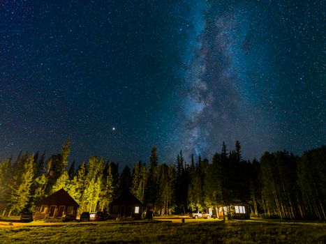 星空下的夜晚，银河在小木屋和森林上方展现出壮丽的景色