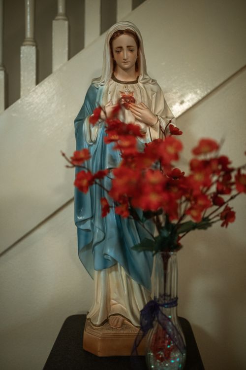 Free Photograph of a Virgin Mary statue adorned with vibrant red flowers in a vase. Stock Photo