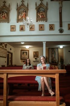 教堂里，两名妇女坐着祈祷，墙上的宗教艺术品营造出宁静的氛围