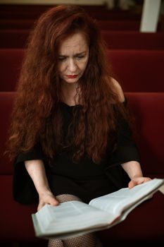 一个女人若有所思地在教堂长座上读着一本书，强调了信仰与灵性